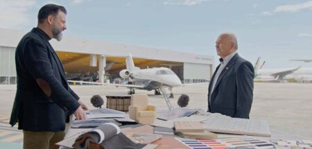 Kadri Muhiddin and Waleed Muhiddin of AMAC Aerospace in conversation over a table of material/design samples with a hangar and aircraft in the background