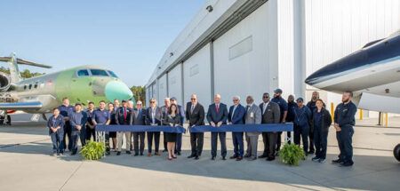 Group photo outside facility with aircraft in background