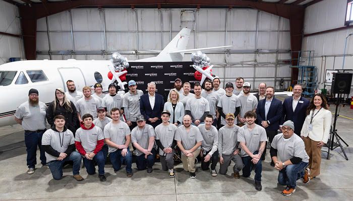 group photo in hangar with aircraft in background