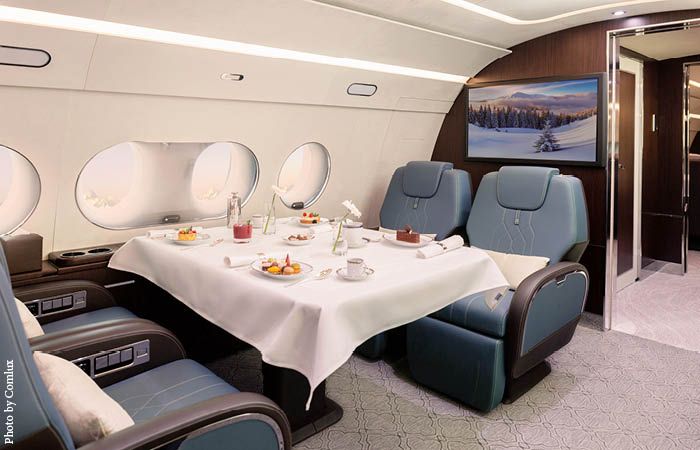 ACJ TwoTwenty cabin. Club four setup with four blue seats around table set for dining