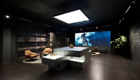 The F/Lab showroom - including central display table with light overhead; large display screen on one wall; seating
