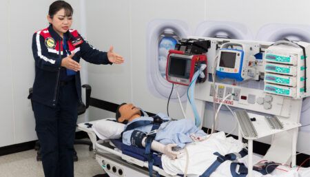 a trainer giving a demonstration stood next to a dummy on stretcher with medical equipment