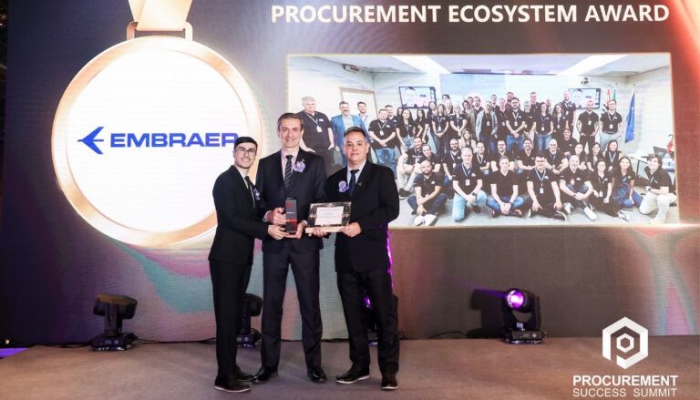 Three people with award in front of screen at the Procurement Success Summit