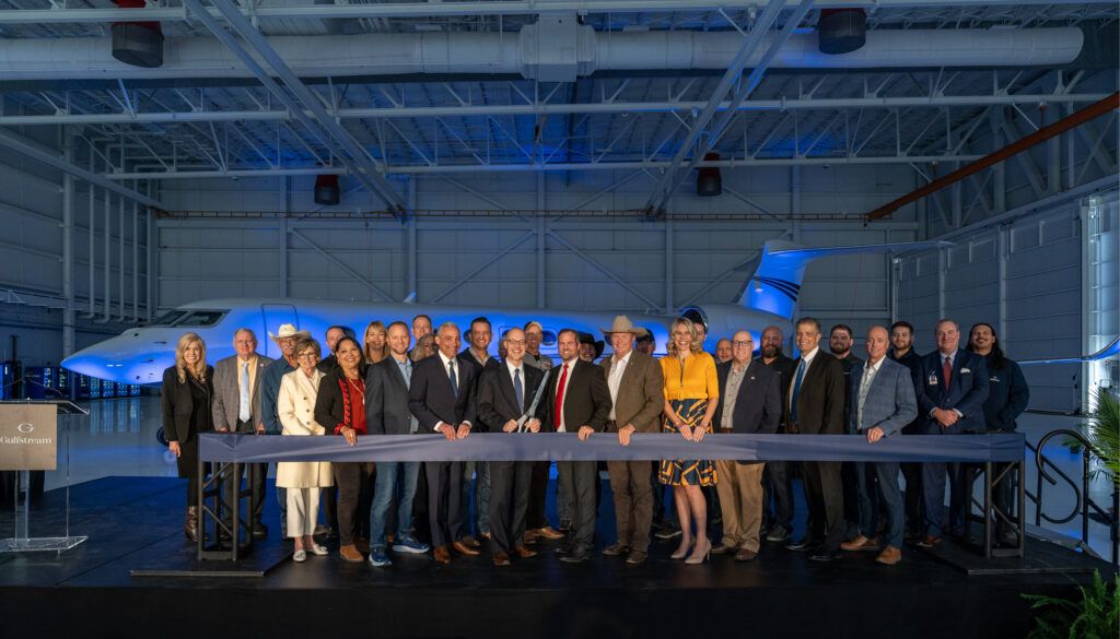 Group of people in front of aircraft in hangar, with ribbon in front