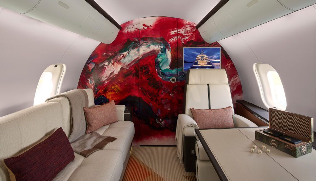 Luxury aircraft cabin with vibrant red abstract artwork on wall and cream leather seating.