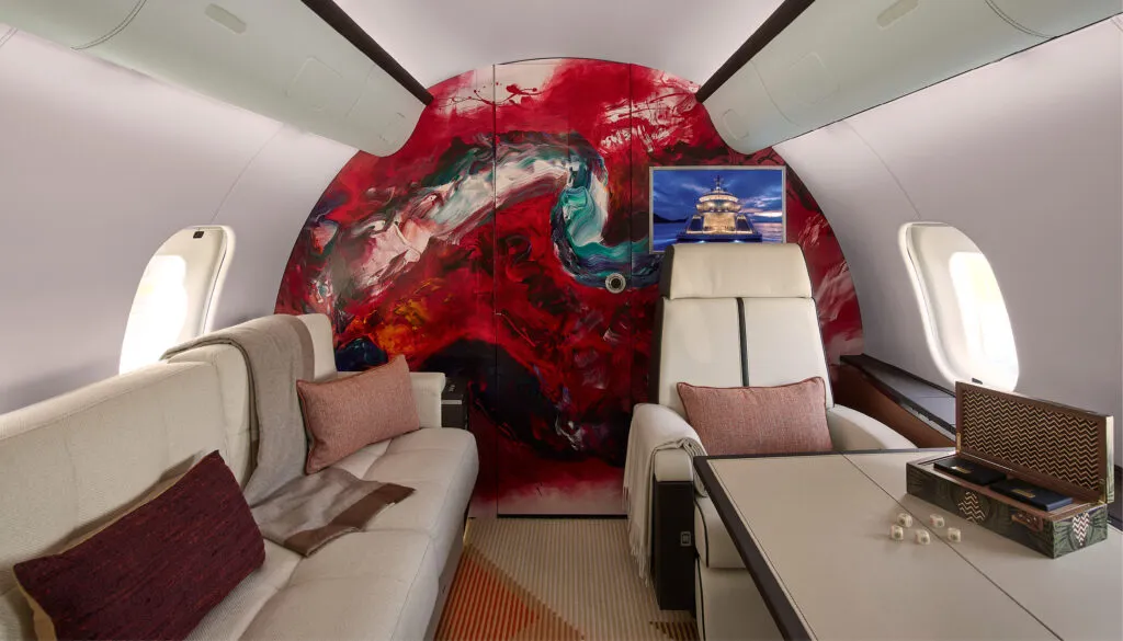 Luxury aircraft cabin with vibrant red abstract artwork on wall and cream leather seating.