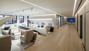 View along the lobby with two business jet cabin mock-ups in foreground, followed by glass-walled room, and large screen and seating in the background.