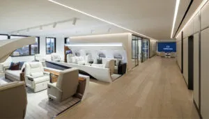 View along the lobby with two business jet cabin mock-ups in foreground, followed by glass-walled room, and large screen and seating in the background.