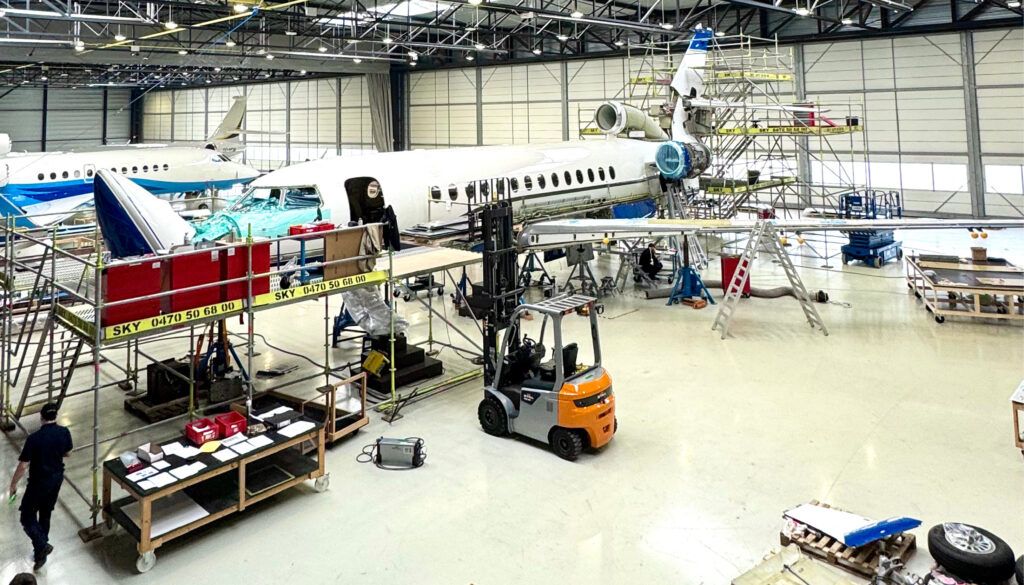 Aircraft hangar with white jet surrounded by scaffolding, tools, and forklift during maintenance