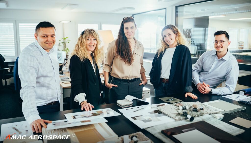 Five people standing behind desk laid out with designs and material samples