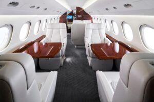 Luxurious private jet interior featuring white leather seats, wood tables, and large windows