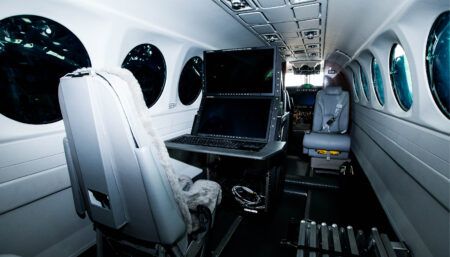 Luxury aircraft interior with leather seats, mission workstation and displays, and oval windows, with view to cockpit beyond