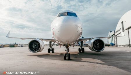 Front view of white aircraft on tarmac showing nose, engines, and landing gear outside hangar building