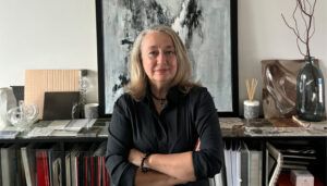 Portrait of Agnès Guiu with material samples, files, and abstract artwork behind her