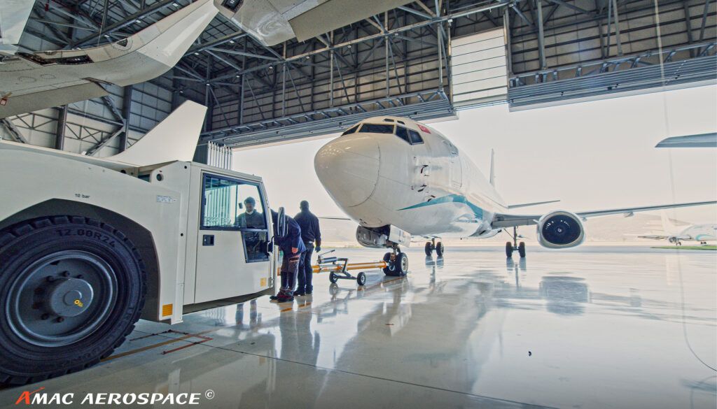 Aircraft maintenance scene inside hangar with technicians working near white plane and ground support equipment