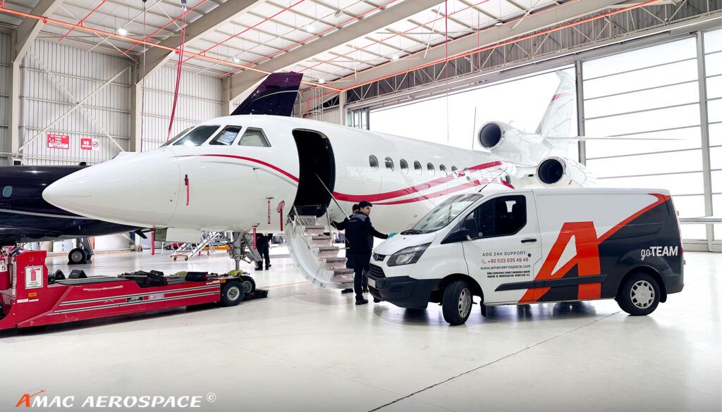 White aircraft with red trim inside hangar with open passenger door and AMAC service van nearby