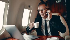 Businessman in suit talking on phone while holding coffee cup on private jet