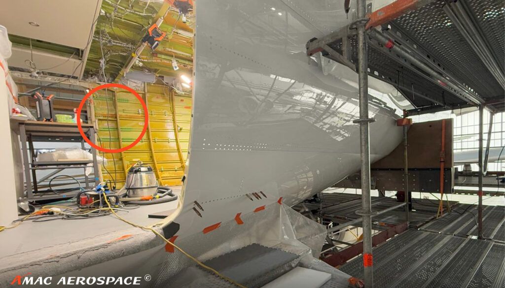 Close-up of aircraft fuselage during maintenance showing scaffolding, yellow panels, and red circular marking highlighting work area