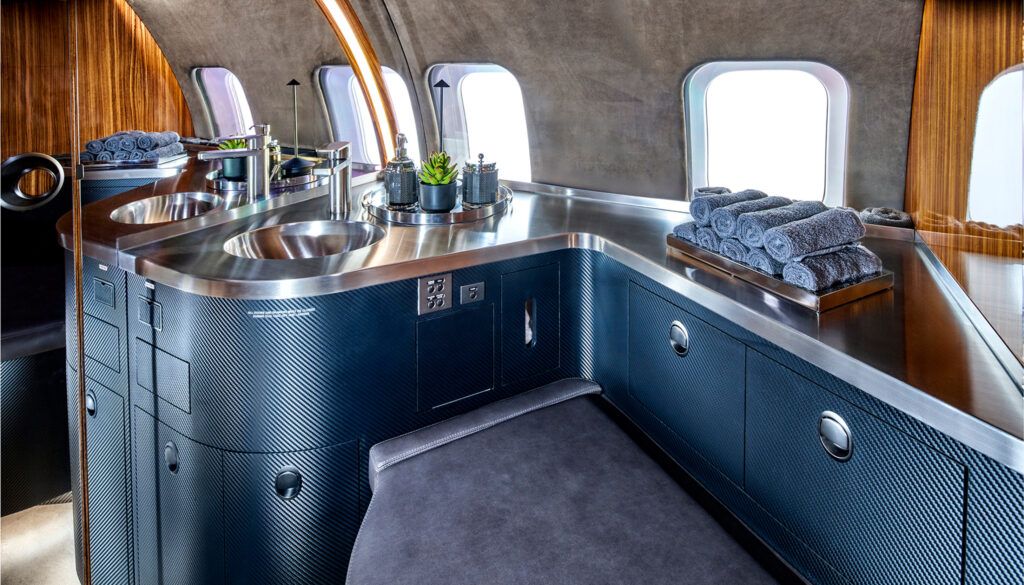 Private jet bathroom with carbon fibre cabinetry, stainless steel sink and countertop, and luxury amenities