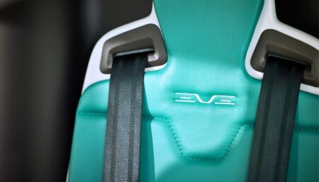 Close-up of turquoise Eve eVTOL seat with safety harness straps and embossed logo