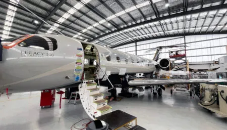 Embraer Legacy 500 aircraft in maintenance hangar with access stairs and equipment nearby