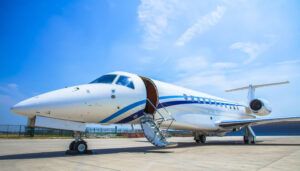 White private jet with blue trim parked on tarmac with passenger door open.
