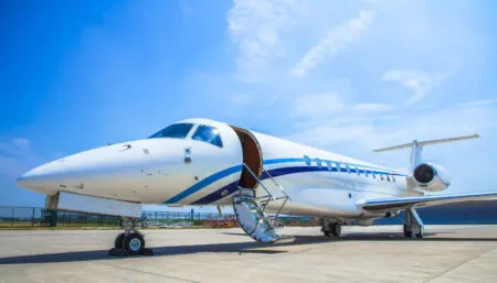 White private jet with blue trim parked on tarmac with passenger door open.