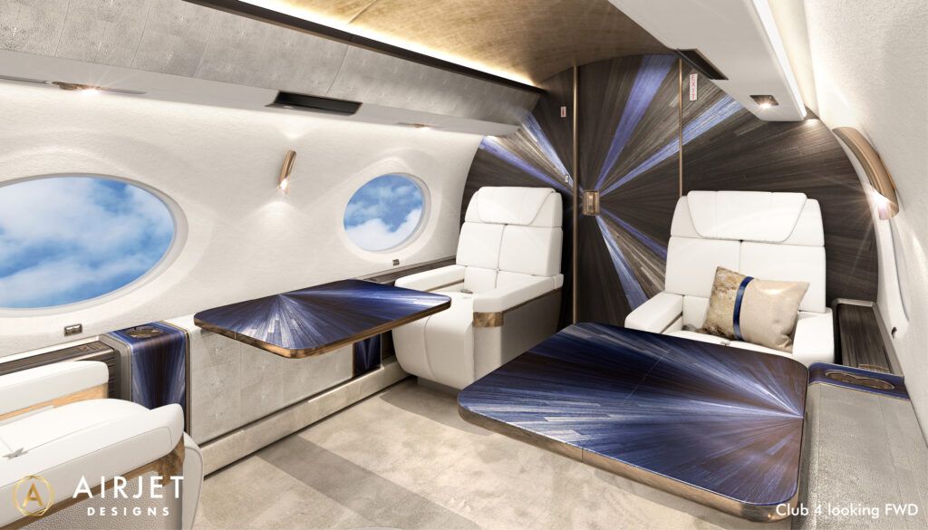 Aircraft cabin with white leather seats, gold accents, and dramatic blue and black sunburst pattern on bulkhead and tables