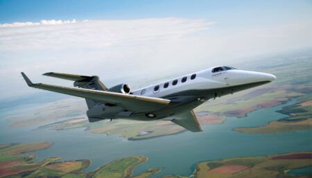 Embraer Phenom 300 private jet flying above land and water