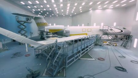 Aircraft in paint booth with maintenance platforms and bright lighting