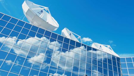 Three white satellite dishes on top of modern office building against blue sky