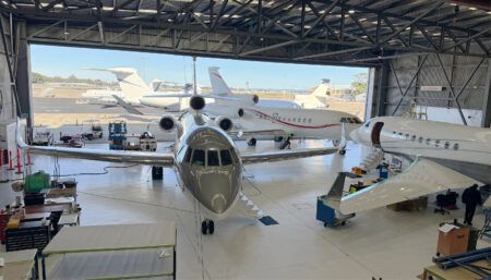 Business jets in hangar with maintenance crew working below