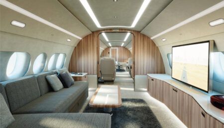 ACJ TwoTwenty interior featuring L-shaped divan opposite large screen on curved credenza with light wood finish
