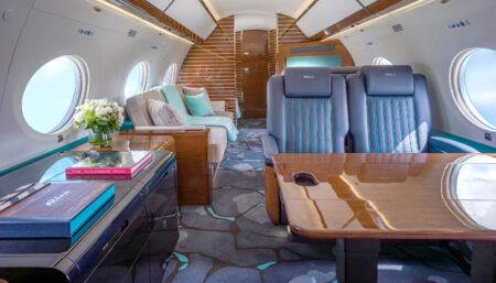 Luxury private jet interior with deep blue leather seats, wooden table, and aquamarine accent details