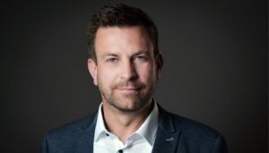 Professional headshot of Fabian Nagel in navy blazer and white shirt against dark background