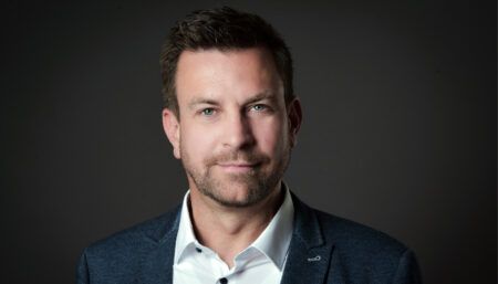 Professional headshot of Fabian Nagel in navy blazer and white shirt against dark background
