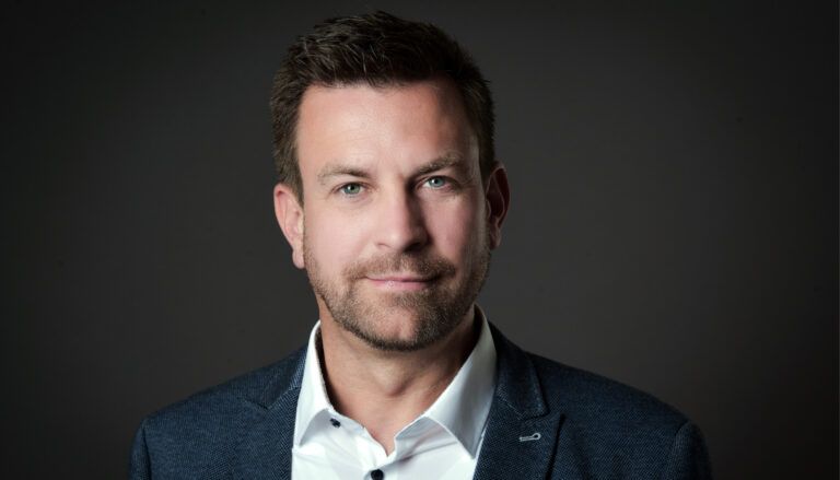 Professional headshot of Fabian Nagel in navy blazer and white shirt against dark background