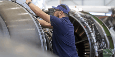 A person in a blue shirt and cap working on the internal components of an aircraft