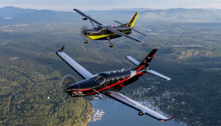 Two aircraft flying over forest landscape with mountains