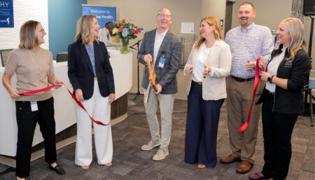 Six people holding red ribbon at healthcare facility opening