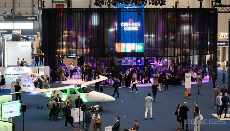 Tradeshow floor with aircraft displays and attendees networking under colourful lighting