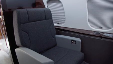 Grey upholstered seat on private jet, next to windows with closed shades