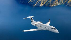 Business jet flying over water near mountainous coastline