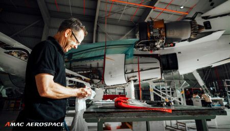 Aircraft maintenance technician working on part in hangar with aircraft in background
