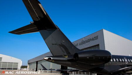 View of tail section of black aircraft outside AMAC Aerospace maintenance facility