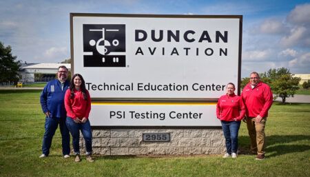 Four people standing by sign for Duncan Aviation’s Technical Education Center