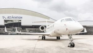 White business jet in front of hangar with aircraft inside