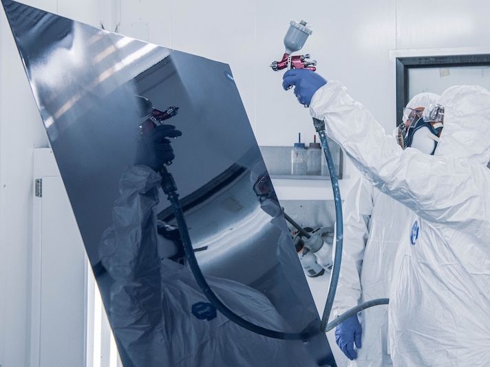 Worker in protective suit spray painting large metal panel