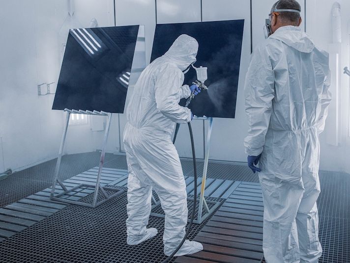 Two workers spray painting panels in industrial paint booth