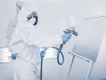 Masked worker spray painting in white protective gear